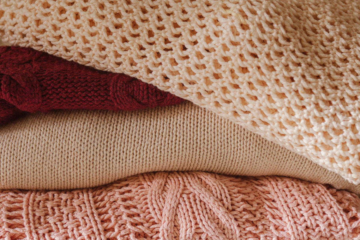 A close-up view of a cozy stack of knitted sweaters in warm shades, emphasizing texture and comfort.