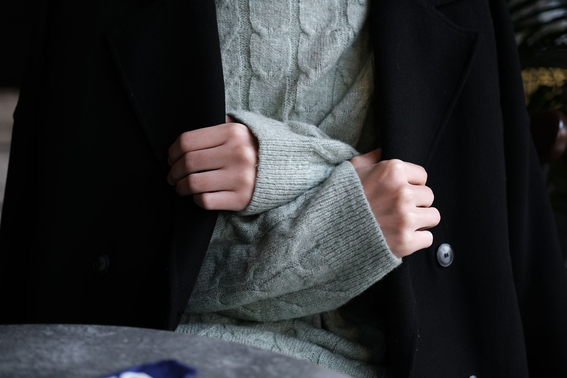Close-up of hands wearing a knitted sweater under a black coat, showcasing winter fashion.