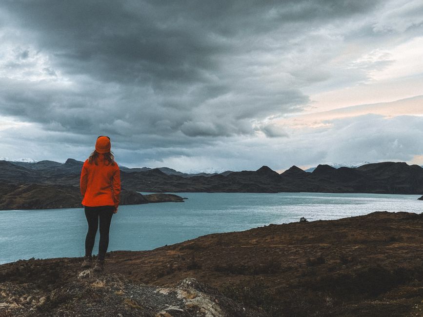 A woman in orange jacket overlooks a dramatic mountain lake in Patagonia, Chile.