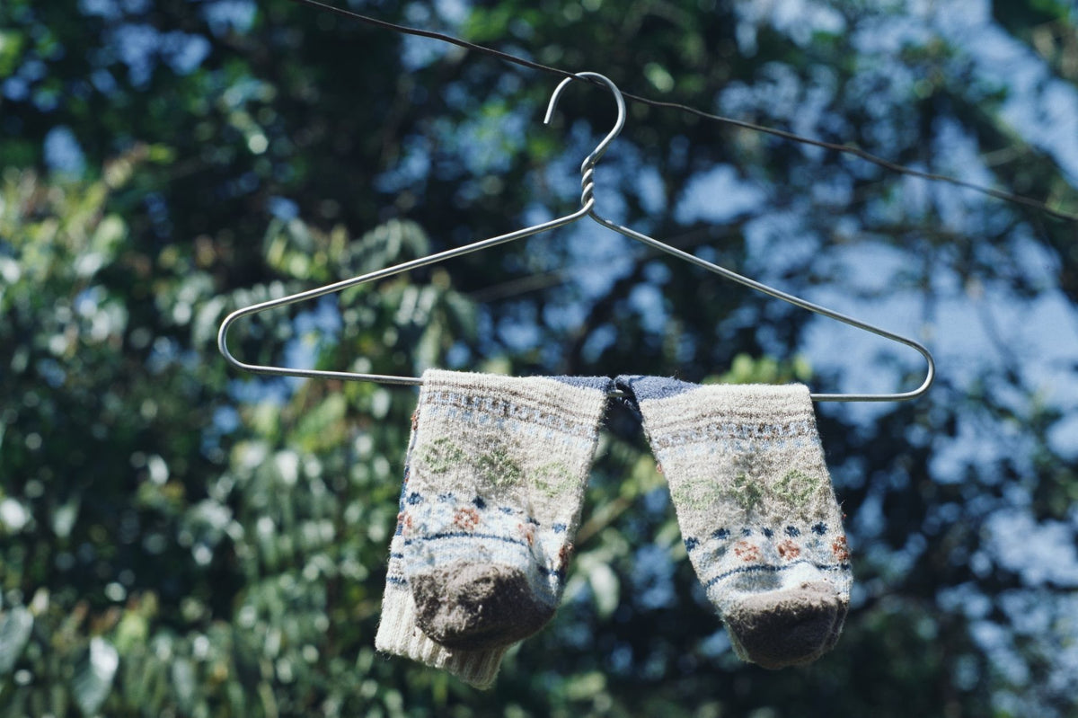 Wool socks hanging on a wire hanger outdoors against a blue sky.