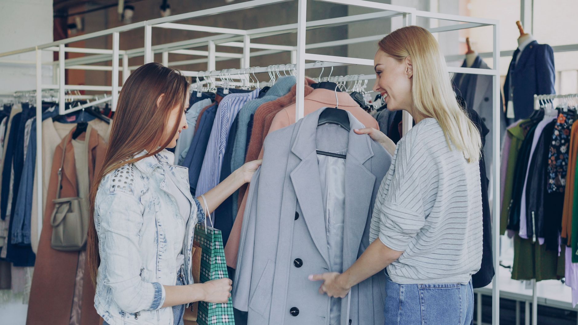 Two women shopping in a clothing store, examining a stylish gray blazer on a rack.