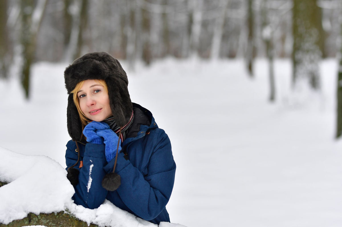 Woman in blue winter jacket and trapper hat enjoying a snowy forest.