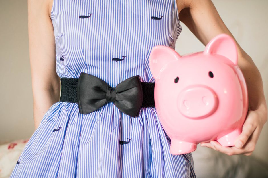 Crop unrecognizable female in lush striped dress with bow on belt with pink piggy bank in hand
